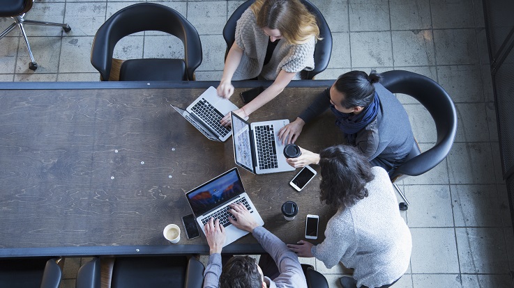 Overheadfoto von vier Personen, die an Computern und Geräten an einem Tisch arbeiten