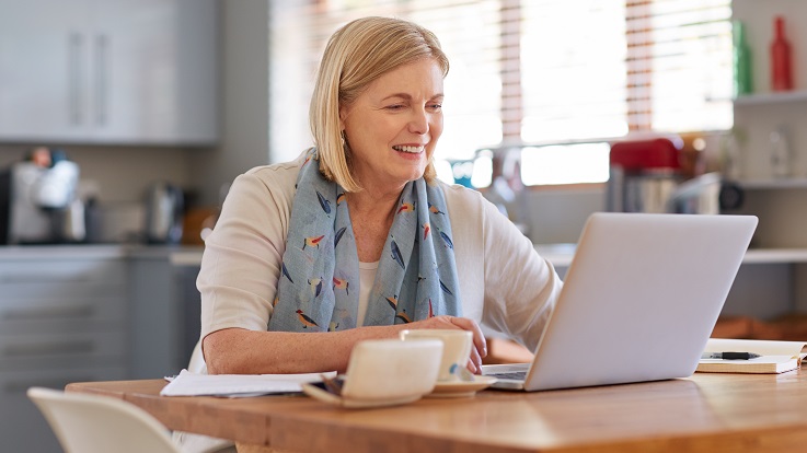 Foto einer Frau an einem Küchentisch, die E-Mails auf einem Computer ansieht
