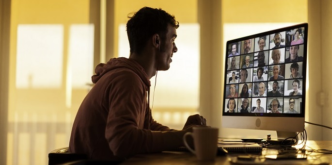 Foto eines Mannes an einem Computer mit einer Videobesprechung auf dem Bildschirm