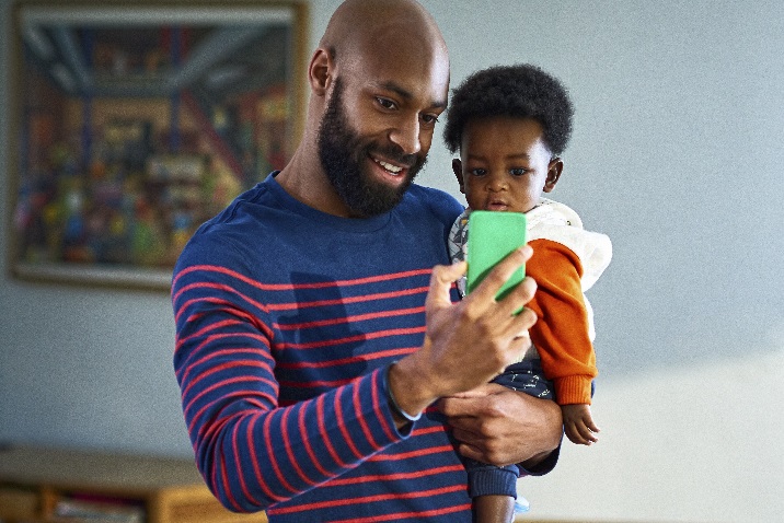 Foto eines Mannes, der ein kleines Kind hält und telefonieren