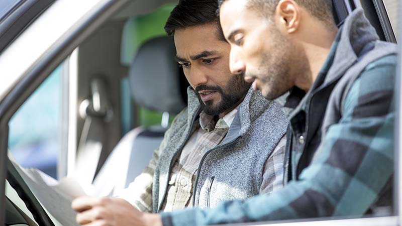 Two men looking at some paperwork - one mane is sitting in a truck drivers seat, the other standing next to him