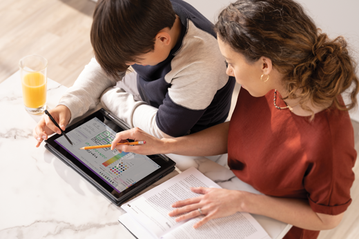 Un enfant de sexe masculin travaille sur une tablette tandis que sa parente regarde par-dessus son épaule
