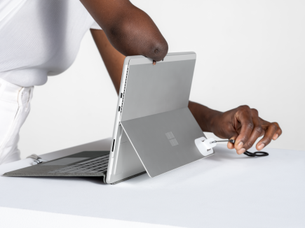 Egy nő az adaptív készlet nyakpánti nyitójával nyitja szét a Surface Pro állványt.