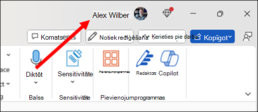 Attēls ar sarkanu bultiņu, kas norāda uz pašreizējo primāro lietotājvārdu, kas atrodas programmas virsrakstjoslā loga augšējā labajā stūrī.