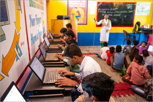 En lærer som presenterer på en skole i India mens elevene arbeider på bærbare datamaskiner.