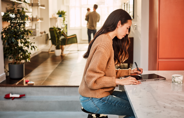 Een vrouw zit aan haar eetkamertafel met haar Lenovo Yoga-computer en pen in tabletmodus.